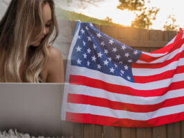 Jovem mulher concentrada em seu laptop em um ambiente interno aconchegante. Atrás dela, uma bandeira americana é exibida em destaque em uma área externa ensolarada, simbolizando alcance global e diversidade cultural.
