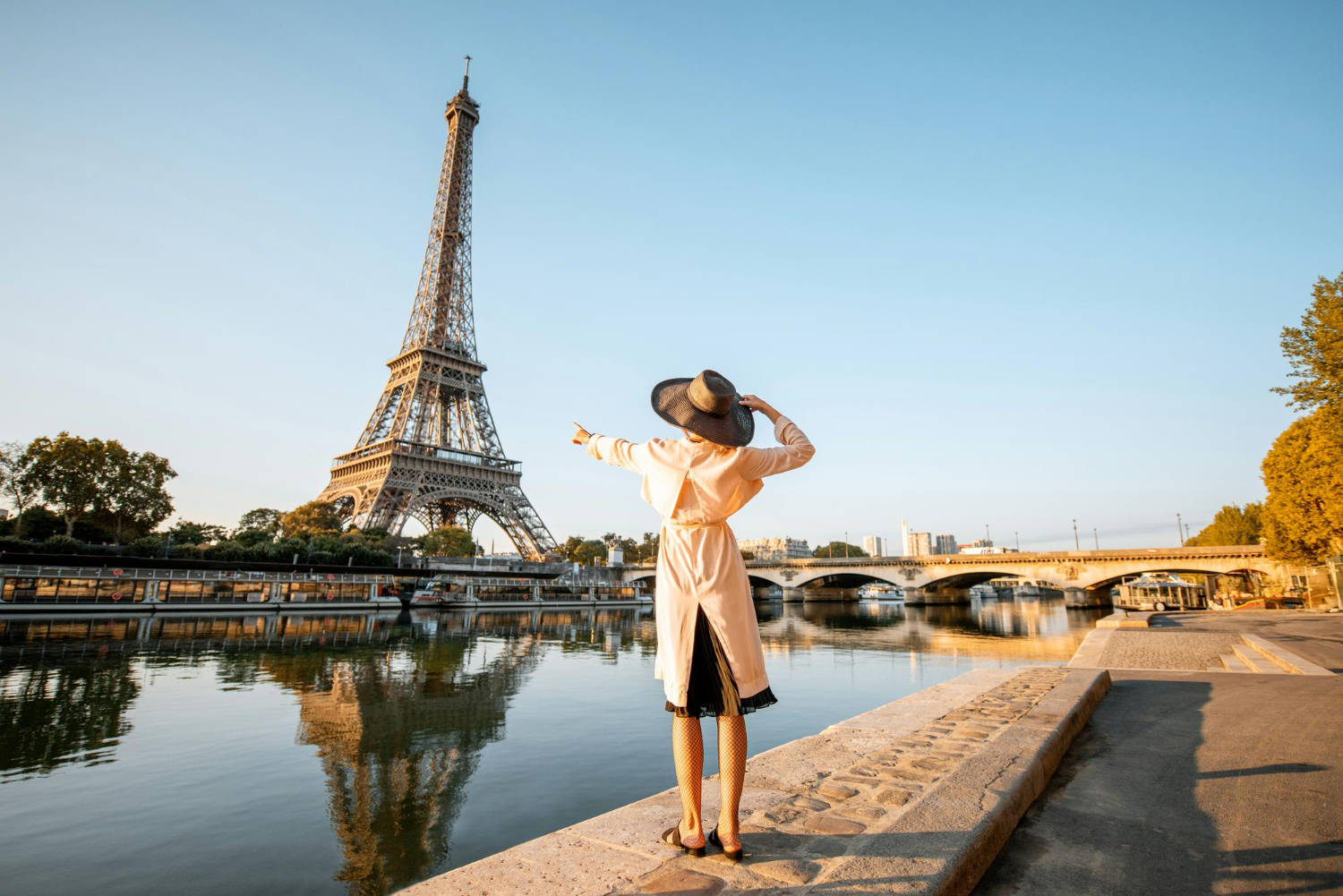 Mulher apontando para a Torre Eiffel ao lado do Rio Sena durante o pôr do sol em Paris.