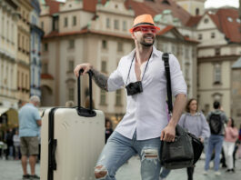 Homem viajante sorridente com malas em uma cidade europeia, representando hospedagem barata e acessível em grandes destinos turísticos