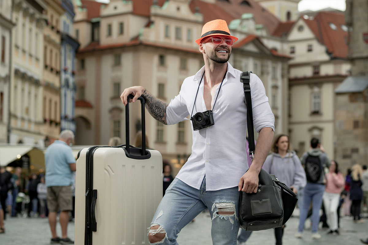 Homem viajante sorridente com malas em uma cidade europeia, representando hospedagem barata e acessível em grandes destinos turísticos