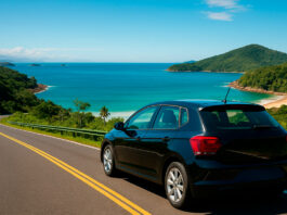 Paraty de carro alugado: explore a Costa Verde com liberdade, conforto e economia Carro moderno em estrada sinuosa da Rio-Santos com vista para o mar e montanhas de Paraty ao fundo, representando viagem pela Costa Verde.