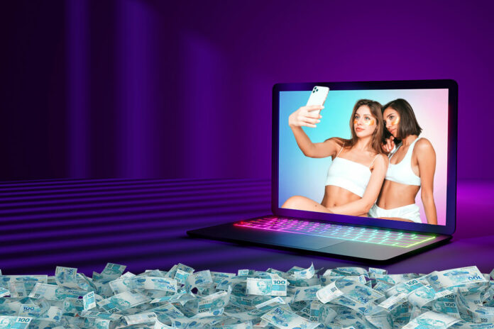 criadoras-conteudo-adulto-dinheiro-online-2025 Criadoras de conteúdo adulto tirando selfie em laptop com cenário neon e cédulas de dinheiro ao redor, representando lucros do conteúdo sensual online