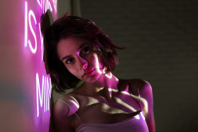 Mulher em ambiente escuro iluminado com luz violeta, olhando para a câmera com expressão sensual e misteriosa, remetendo a lives premium em 2025