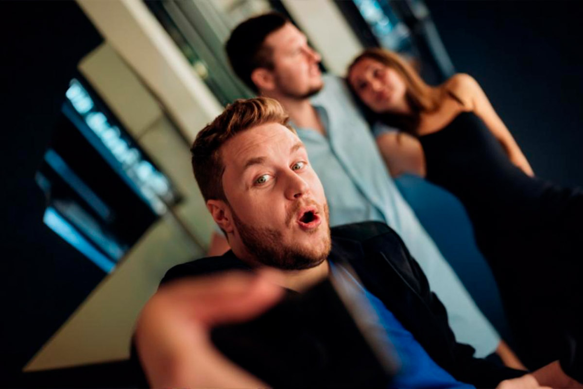 Homem surpreso em primeiro plano enquanto observa um casal junto ao fundo, representando a dinâmica de casais liberais que buscam novas experiências.