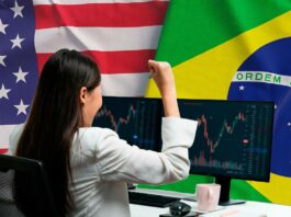 Mulher comemorando ganhos em investimentos com gráficos na tela, bandeiras dos EUA e do Brasil ao fundo.