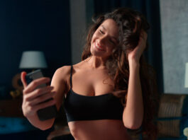 Mulher sorridente fazendo selfie em casa, representando transmissão ao vivo para ganhar dinheiro no Chaturbate