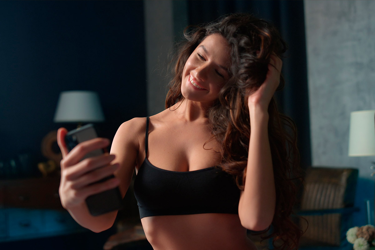 Mulher sorridente fazendo selfie em casa, representando transmissão ao vivo para ganhar dinheiro no Chaturbate